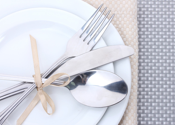 White empty plates with fork, spoon and knife tied with a ribbon on a grey tablecloth - Foto, afbeelding