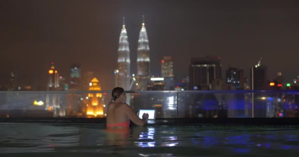 Vista della donna in piscina sul tetto del grattacielo utilizzando tablet contro paesaggio notturno della città. Kuala Lumpur, Malesia
 - Filmati, video