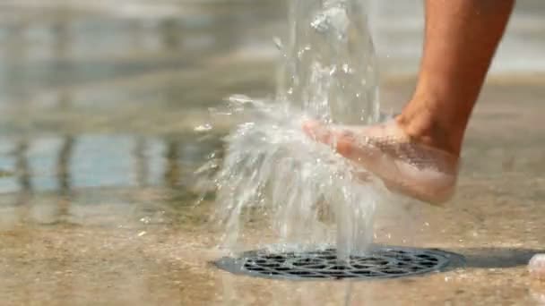 Wasser strömt aus dem Boden. Der menschliche Fuß spielt mit Wasser. fällt das Wasser auf den Boden. Nahaufnahme - Filmmaterial, Video