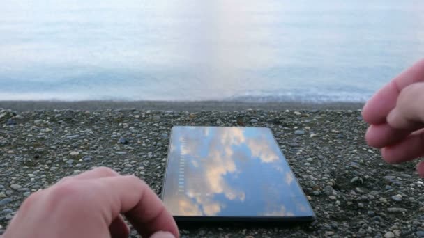 A mobil telefon szól a kavicsos strandtól, az óceán. Férfi keresi a fényképeket. Közeli kép:. - Felvétel, videó