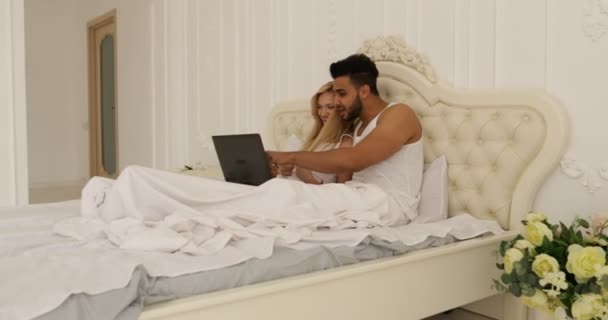 Couple lying bed using laptop computer, mix race man woman smile morning bedroom - Imágenes, Vídeo