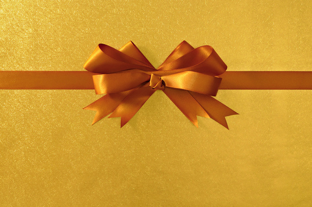Gold gift bow and ribbon, shiny metallic foil paper background,  - Φωτογραφία, εικόνα