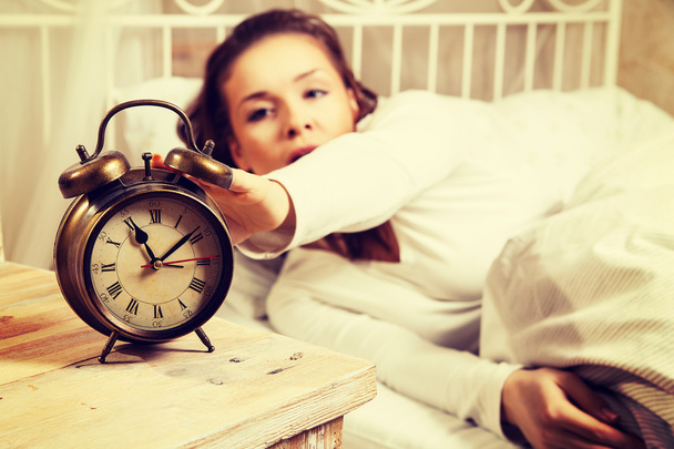 Woman in bed turning off alarm clock - Photo, image