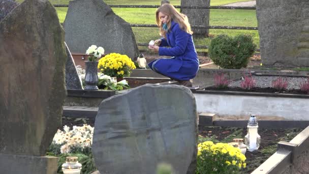 Young woman lights candle lantern in memory of husband father in cemetery. 4K - Footage, Video