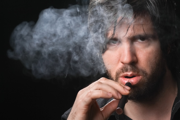 Młody człowiek palenia papierosów elektronicznych na czarnym tle - Zdjęcie, obraz