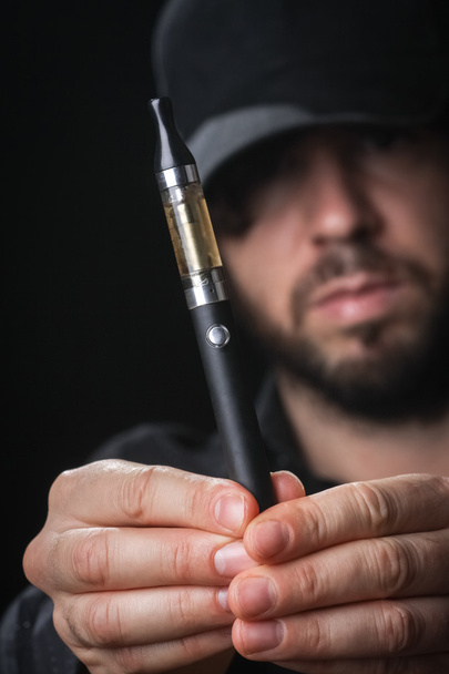 Young man smoking electronic cigarette on black background - Zdjęcie, obraz