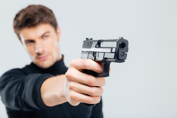 Closeup of focused young man standing and aiming with gun - Fotoğraf, Görsel