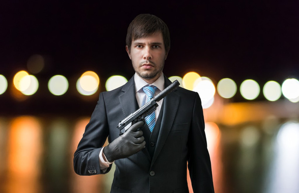 Agent or spy holds pistol in hand at night. Blurred lights in background. - Photo, Image