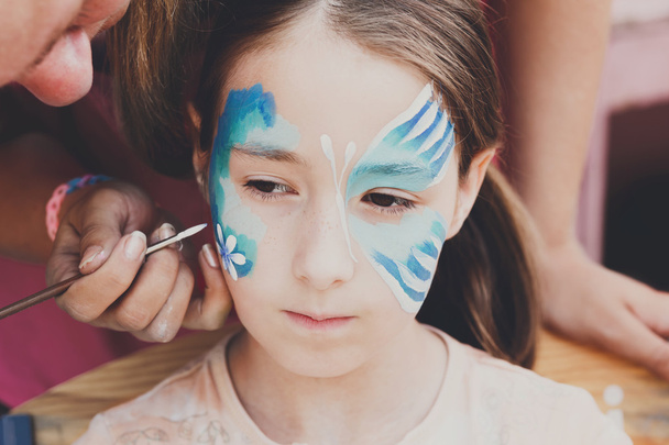 Feminino criança rosto pintura, fazendo processo de borboleta
 - Foto, Imagem