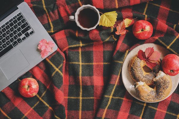 Top view of cozy autumn morning at home. Breakfast with laptop, cup of tea and bagel with apples on woolen plaid blanket. Working at home. - Foto, immagini
