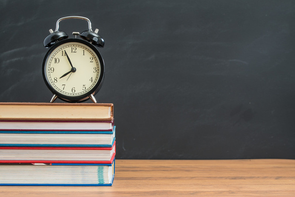 alarm clock and book on student desk in front of blackboard - Foto, Imagen