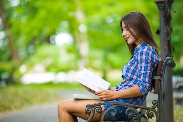 Kolegium dziewczyna trzyma książkę siedzą w parku - Zdjęcie, obraz