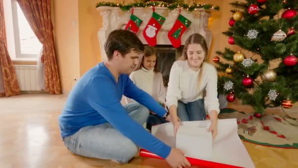 Onnellinen perhe istuu lattialla ja käärii joululahjoja paperiin ja koristelee nauhoilla
 - Materiaali, video