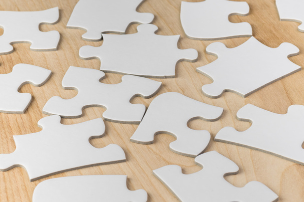 Plain white jigsaw puzzle pieces on a wooden table. - Valokuva, kuva