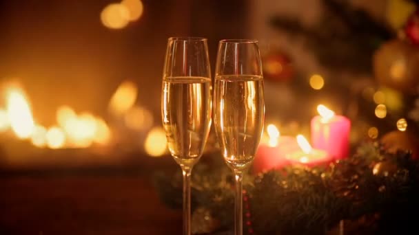 Primer plano de dos copas de champán gaseoso frente a la chimenea en llamas. Árbol de Navidad decorado y velas encendidas en el fondo
. - Imágenes, Vídeo