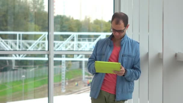Programmer in black rim glasses using his tablet computer at modern railroad station - Filmati, video