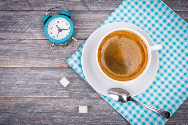 Cup of coffee on saucer with spoon. Blue napkin and alarm clock - Photo, Image