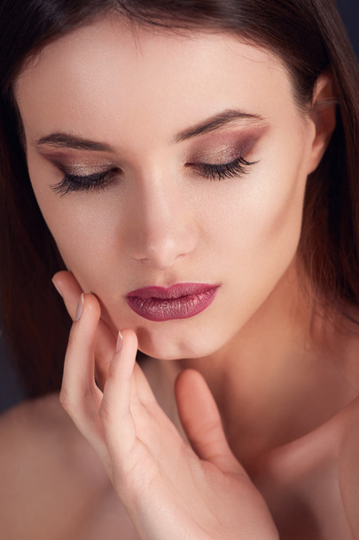 Young woman with beautiful healthy face with purple lipstick and bronze manicure.Beautiful young woman with clean skin of the face. Perfect Make-up closeup. Girl with Perfect Skin. Dark background - Zdjęcie, obraz