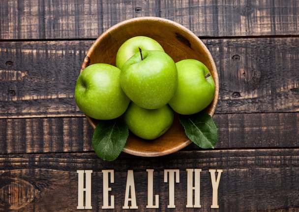 Green organic healthy apples in bowl on wooden board - Фото, изображение