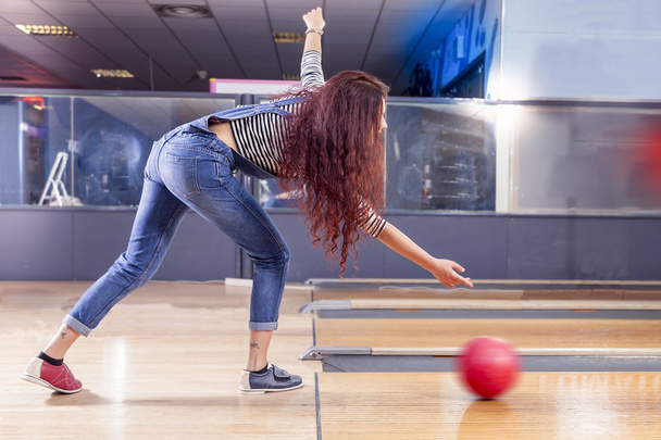 jong meisje trekt de bal op de bowlingbaan - Foto, afbeelding
