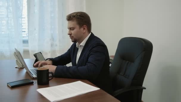 Jonge zakenman in zijn kantoor voorkant van de laptopcomputer werkt, dan hij op zijn horloge kijkt begrijpt dat hij te laat is voor een bijeenkomst zijn spullen neemt en gaat weg - Video