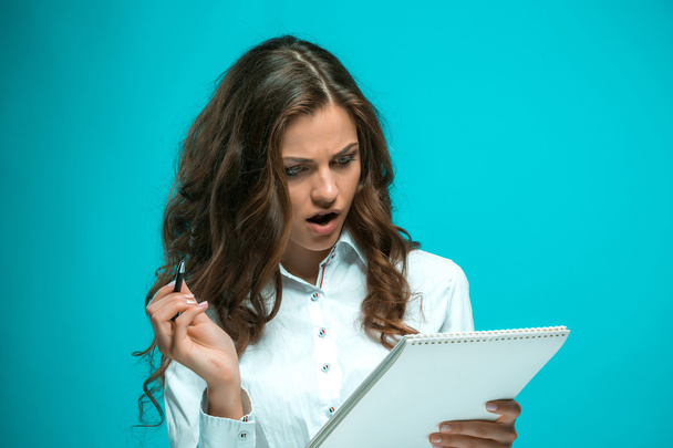 Yllättynyt nuori liiketoiminnan nainen kynä ja tabletti muistiinpanoja sinisellä taustalla
 - Valokuva, kuva