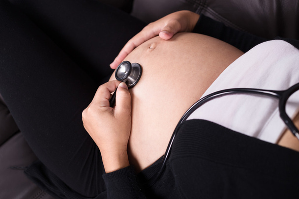 close up pregnant woman listening baby's heartbeat with stethosc - Foto, imagen