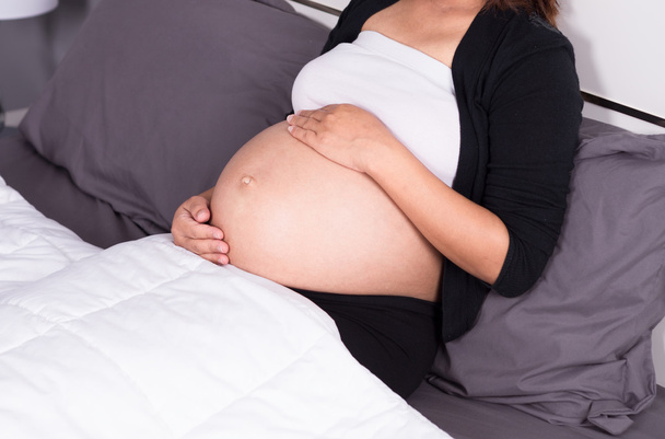 close up belly of pregnant woman sitting on bed in the bedroom - Photo, Image