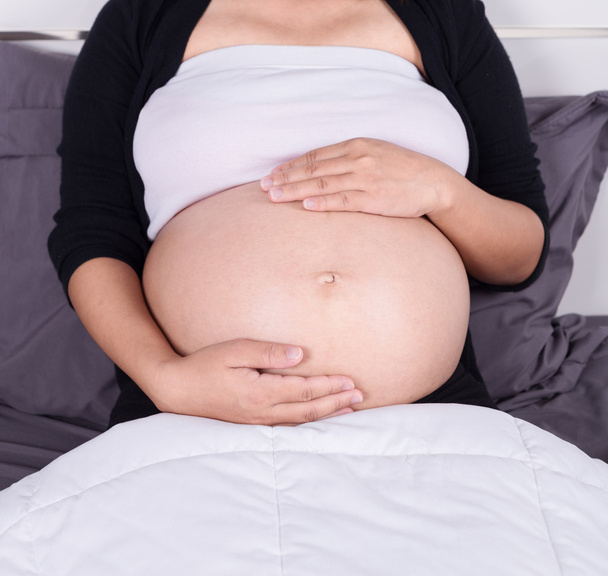 close up belly of pregnant woman sitting on bed in the bedroom - Фото, изображение
