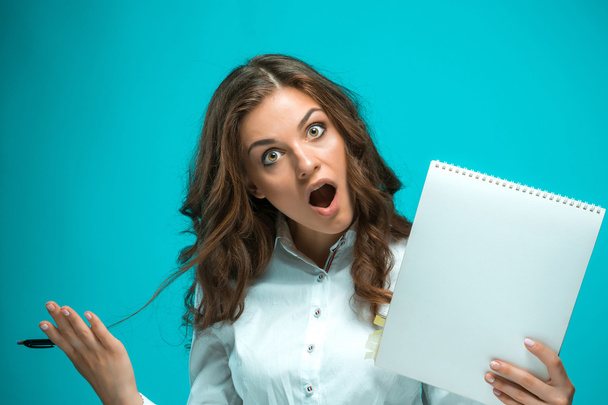 Surprised young business woman with pen and tablet for notes on blue background - Fotoğraf, Görsel