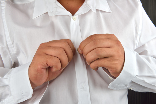Young man buttoning his white shirt on a dark background. He is  - Photo, image