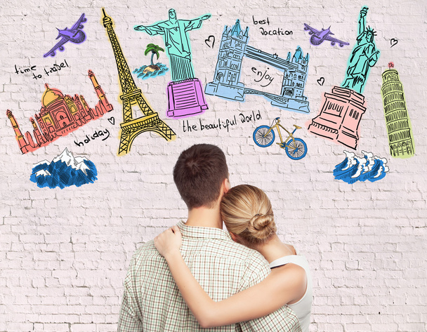 Young caucasian couple looking at creative travel sketch on brick background. Traveling concept - Fotoğraf, Görsel