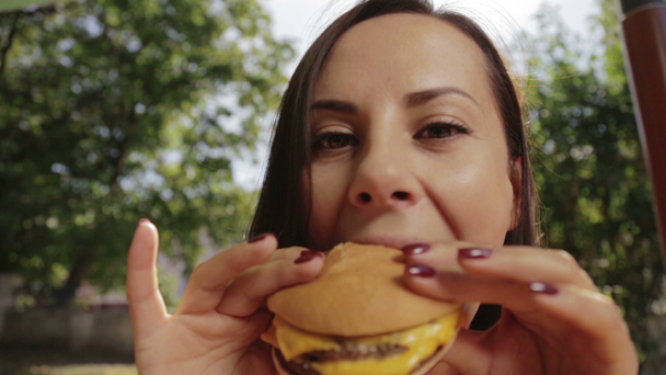 Portrét dívky close-up s hamburger v ruce. Mladá krásná žena jíst hamburger v kavárně. - Záběry, video