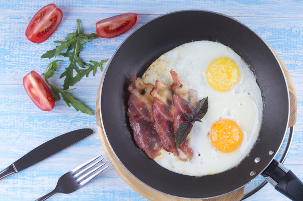 Fried egg with bacon and tomatoes on a wooden background - 写真・画像