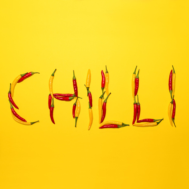 Red hot chili peppers on yellow background making word " CHILLI" - Zdjęcie, obraz