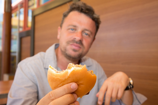 Homem no restaurante comendo um hambúrguer, ele está com fome
 - Foto, Imagem
