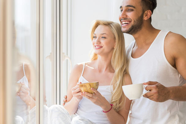 Young Beautiful Couple Stand Near Big Window, Drink Morning Coffee Cup, Happy Smile Hispanic Man And Woman - Фото, зображення