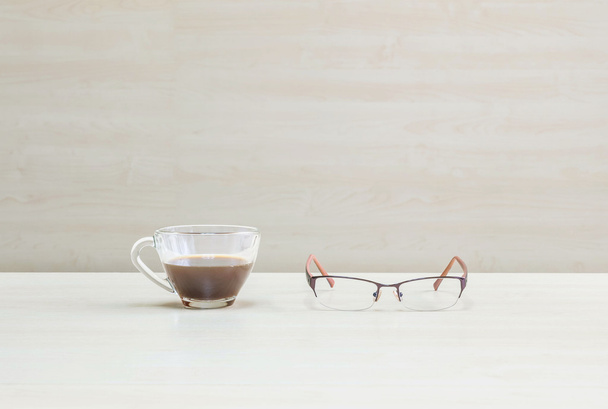 Крупный план черный кофе в прозрачной чашке кофе с очками на размытом деревянный стол и стены текстурированный фон в конференц-зале под окном света
 - Фото, изображение