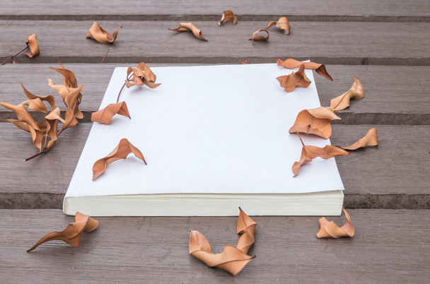 Kniha s bílou poznámkou na dřevěném stole v zahradě se sušenými listy s texturovou tapetu - Fotografie, Obrázek