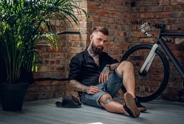 Maschio hipster tatuato si siede su un pavimento
 - Foto, immagini