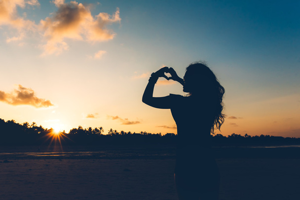 silhouette of sexy brunette in fashion swimwear making hand gestures, showing love at sunset - Foto, imagen