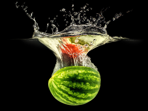 Fresh melon falling in water with splash on black background - Fotó, kép