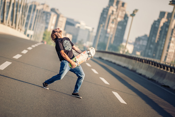 Feliz skatista na ponte tocando guitarra em seu skate
  - Foto, Imagem