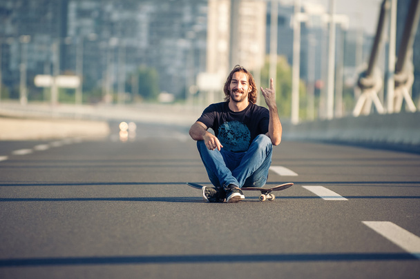 Skateboarder sitting on his skateboard at highway bridge - Фото, изображение