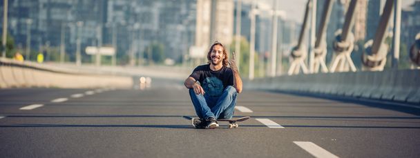 Skateboarder sitting on his skateboard at highway bridge - Photo, Image