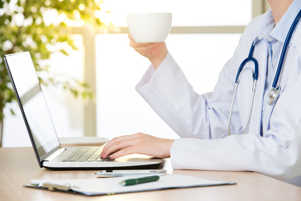 Doctor using computer to research internet and drink coffee - Foto, imagen