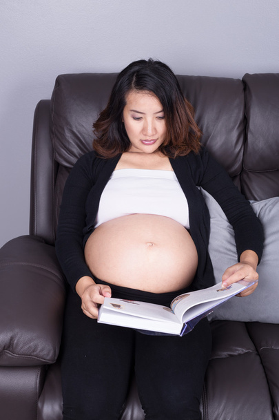 pregnant woman lying on sofa and reading book - Foto, afbeelding