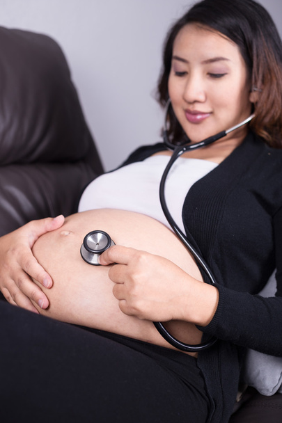 pregnant woman listening baby's heartbeat with stethoscope on he - Фото, изображение