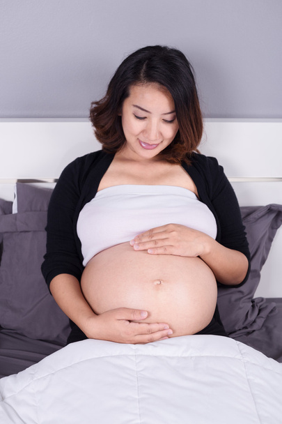 беременная женщина смотрит на свой живот, лежа на кровати
 - Фото, изображение