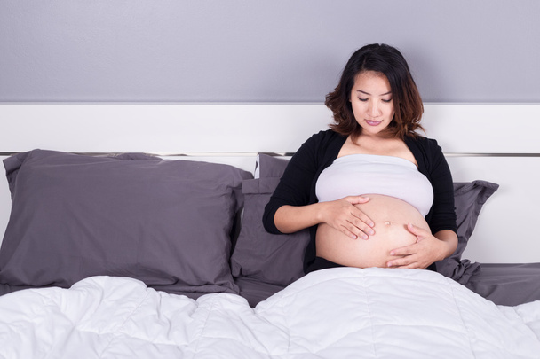 pregnant woman looking at her belly while lying on bed - Foto, immagini